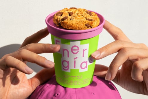 Colorful to-go cup with vibrant branding, topped with a cookie. Perfect for packaging design mockups, creative marketing, and food branding projects.