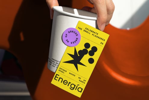 Hand holding coffee cup with a bold yellow tag and purple sticker mockup design, featuring modern graphics and typography for designers seeking inspiration.