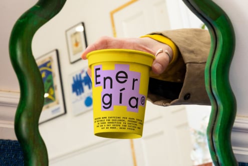 Hand holding a yellow coffee cup labeled Energia, stylish modern kitchen background, vibrant design. Ideal for graphics, mockups, packaging templates.