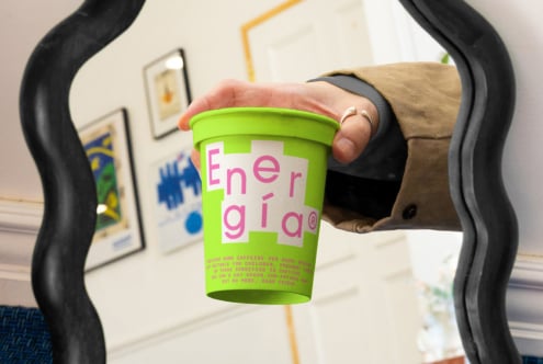 Hand holding a green cup labeled Energia with colorful typography in an interior space. Graphic design, templates, mockups, creative assets for designers.