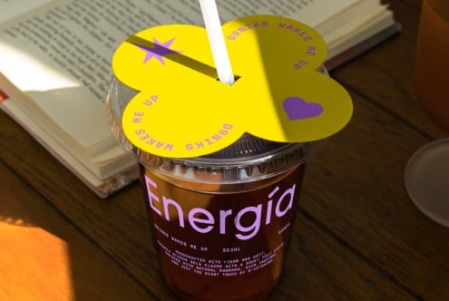 Energy drink cup with vibrant yellow lid and heart design beside an open book, ideal for mockup templates, graphic design, vibrant packaging concepts.