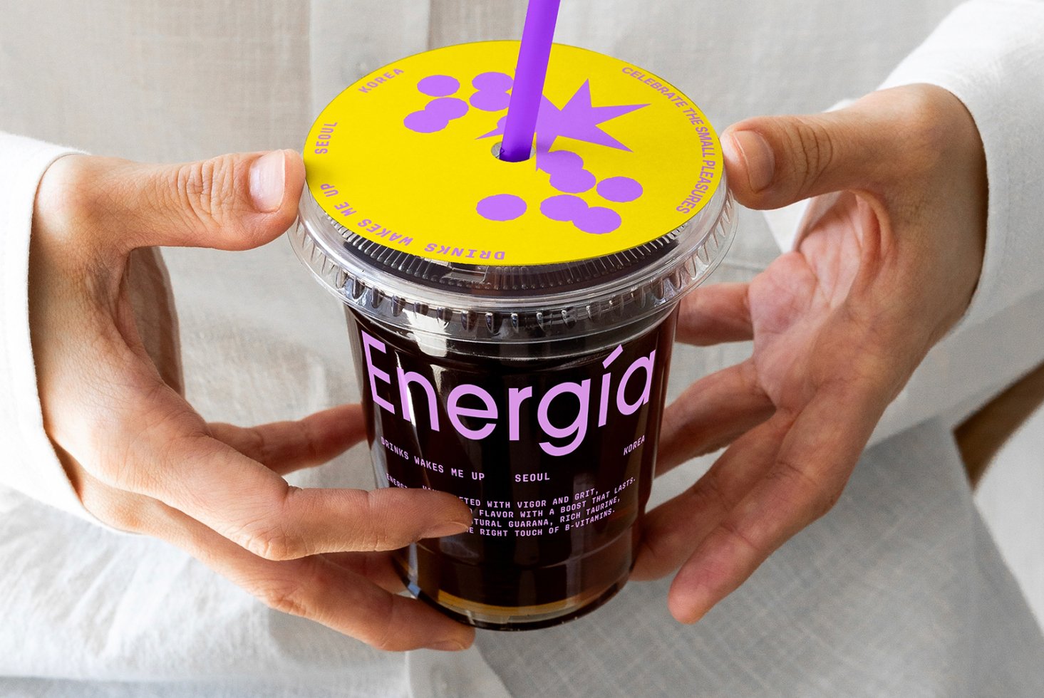 Hands holding a vibrant coffee cup with a yellow lid and purple design. Bold font reads Energia. Perfect for branding, packaging mockups, graphic design.