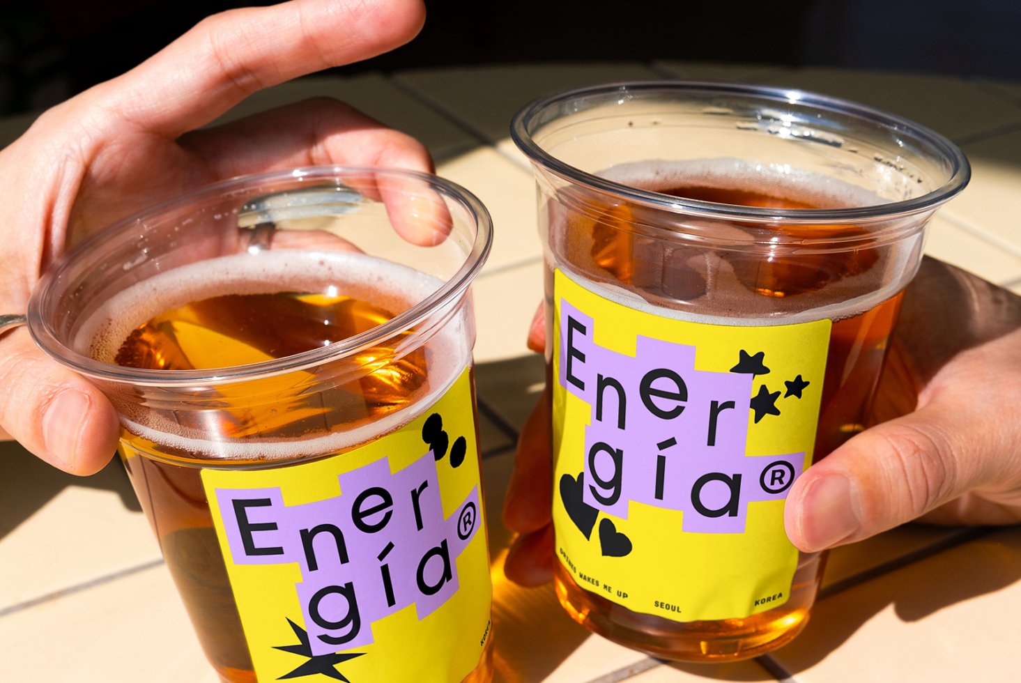Two hands hold clear cups with vibrant designs saying Energia ideal for mockup templates suitable for graphic design projects and branding purposes.