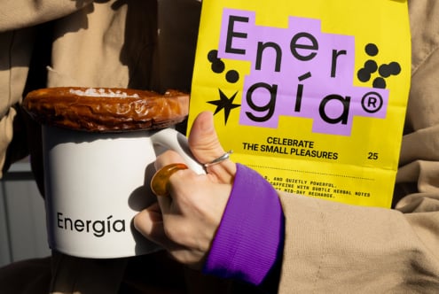 Person holding yellow packaging design with text Energia and white mug topped with caramel donut perfect for branding mockups and graphic design inspiration