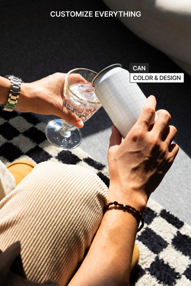 Mockup image of hands holding a customizable can and a glass on a checkered rug. Perfect for designers seeking unique product design templates and inspiration.