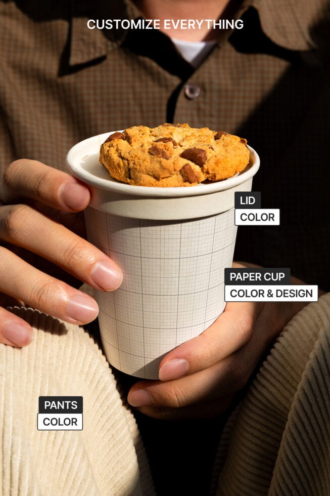 Hands holding customizable paper cup mockup with cookie lid. Ideal for branding, packaging design. Keywords: mockup, customizable, branding, design.