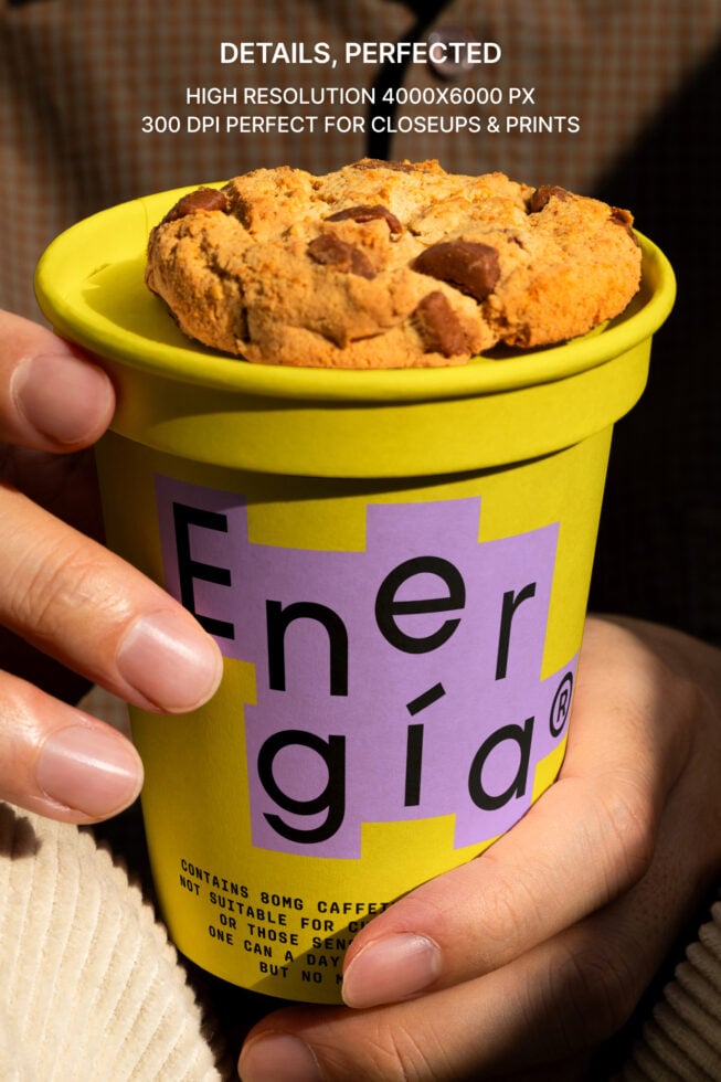 Hand holding a yellow cup with a cookie on top featuring a purple label with modern typography. Ideal for packaging mockups and branding templates.