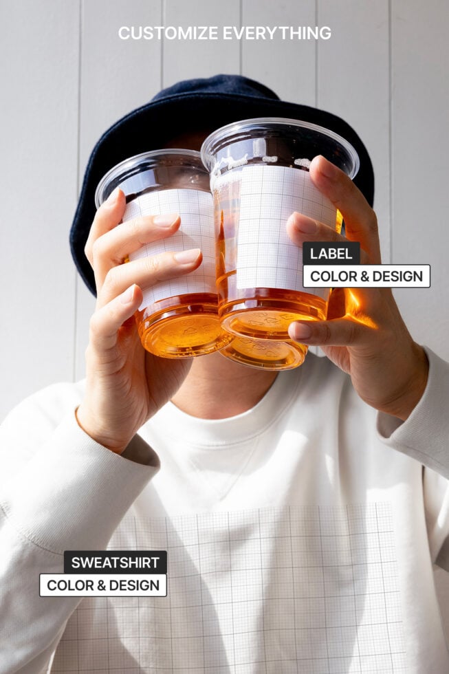 Person holds two drinks with customizable labels and sweatshirt. Keywords: customizable labels, sweatshirt design, mockup, digital design asset.
