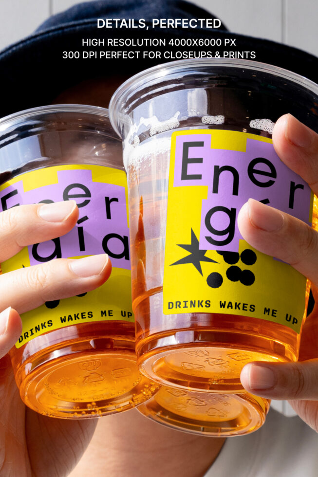 Hands holding two energy drink cups with bold purple and yellow labels featuring edgy font. Perfect for print projects, branding, and packaging design.