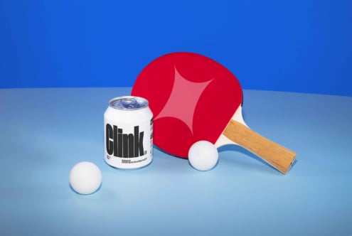 Table tennis paddle with red rubber, two white balls, and a Clink soda can on blue background. Ideal for mockups, product design, sports graphics.