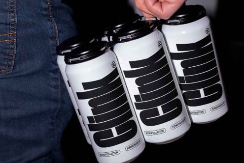 A hand holds a pack of four white cans with bold black text design labeled clink suitable for branding mockups in digital asset marketplace for designers.