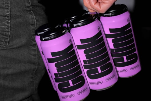 Hand holding a set of four purple beverage cans showing bold black typography design. Perfect for packaging mockups, graphic resources, and templates.