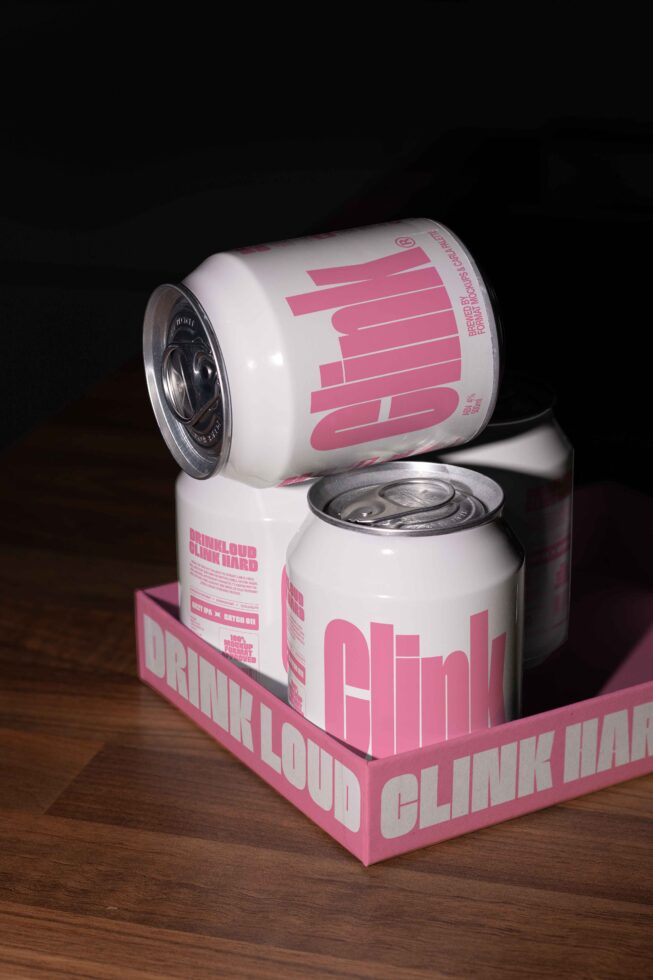 Cans with bold pink typography in a tray on wooden surface mockup. Perfect for graphic designers needing packaging design inspiration and drink branding.