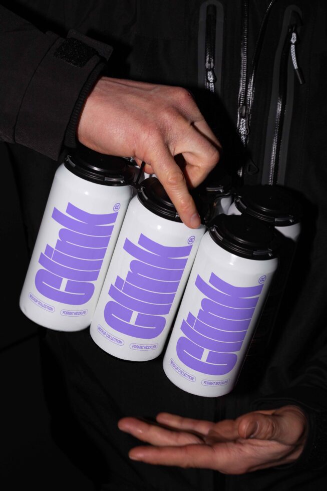 Design mockup featuring a hand holding four white beverage cans with bold purple typography ideal for branding projects and graphic design templates.