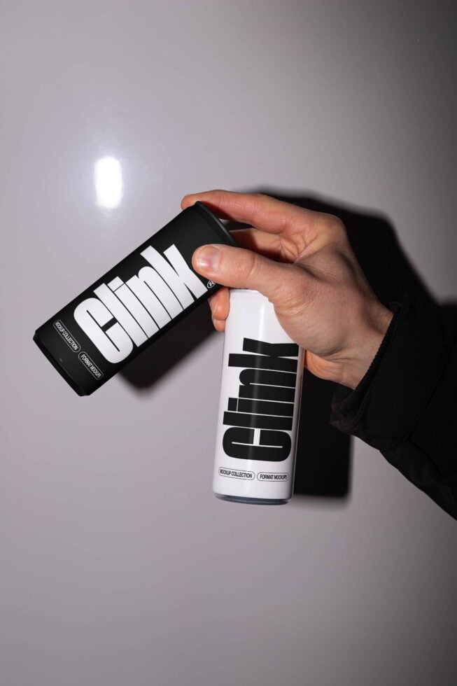 A hand holding black and white Clink branded spray cans, ideal for mockup demonstrations in design projects. Packaging design, product mockups, creative assets.