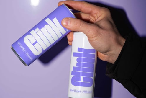 Hand holding two Clink beverage cans with modern design mockup, ideal for branding mockups, showcasing bold typography and creative packaging design.