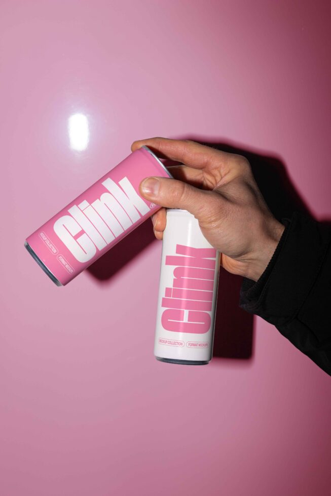 Hand holding pink and white can mockups with Clink branding against a pink background. Ideal for beverage design presentations and marketing assets.