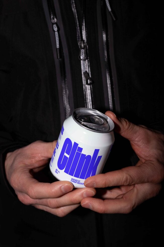 Person holding a soda can with blue Clink branding against a dark jacket. Ideal for packaging mockup designs and brand presentations.