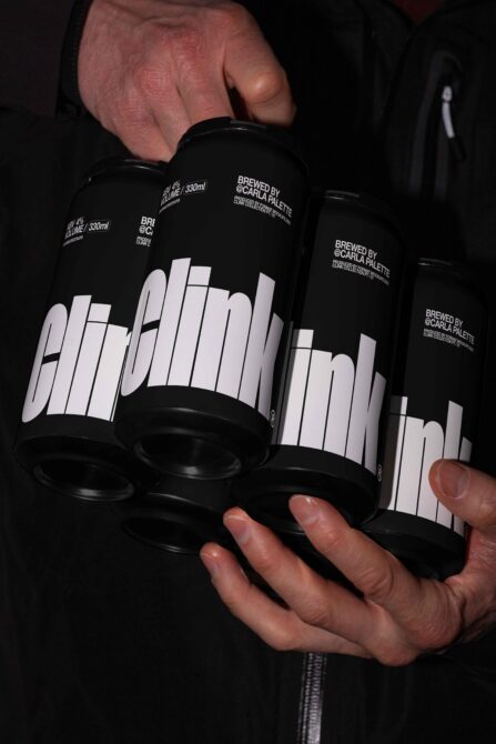 Hands holding three black cans with white geometric logo in dark lighting