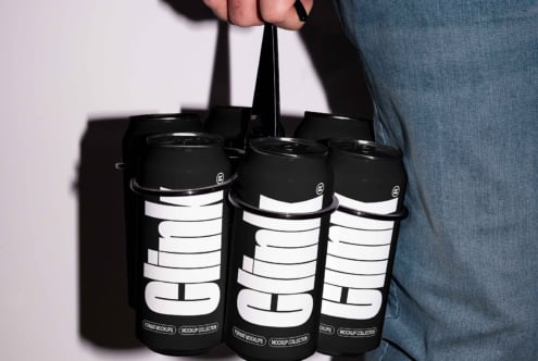 Mockup of a hand holding six-pack black cans with bold typography design, ideal for showcasing product branding. Perfect for designers, ads, templates.