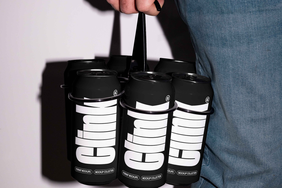 Person in denim holding black six pack carrier with white geometric logo design