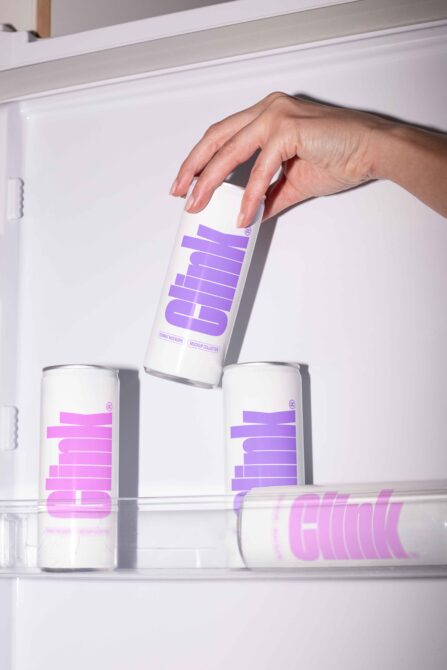 Hand holding tall white can with purple geometric logo design in shelf setting