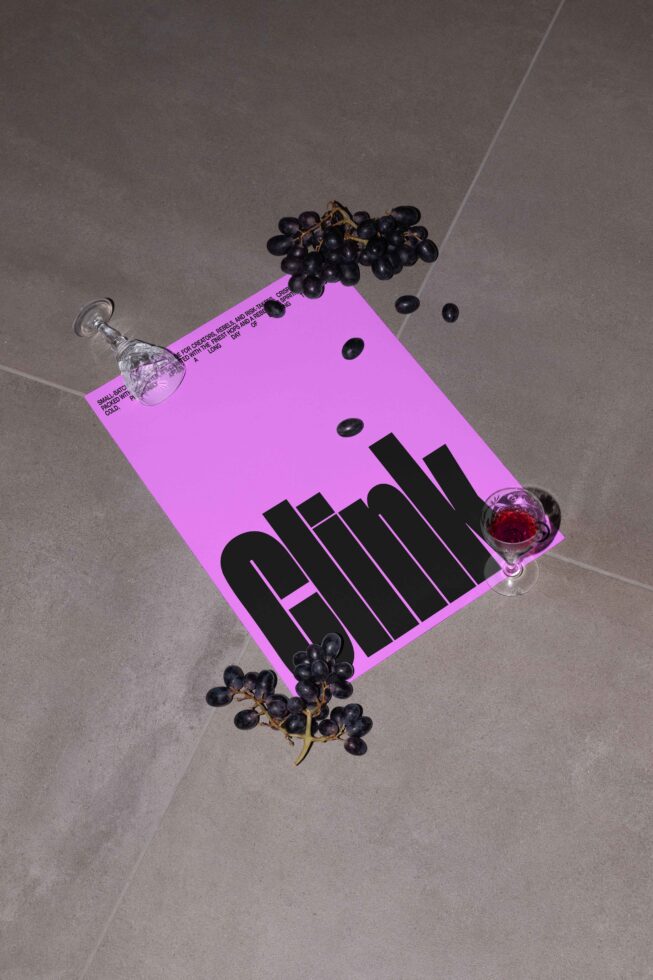 Pink poster mockup with bold black typography placed on a gray surface, surrounded by grapes and a small wine glass; perfect for designers.