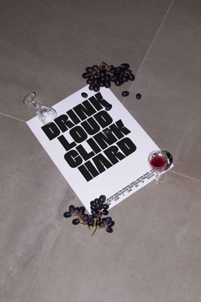 Bold typography poster with the text Drink Loud Clink Hard on a grey background. Surrounded by a wine glass and grapes. Ideal for creative mockups.