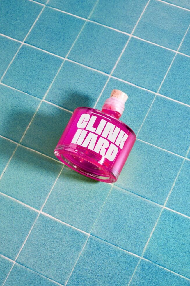 Pink bottle with bold white text Clink Hard on turquoise tiled surface perfect for mockup or branding projects ideal for designers seeking vibrant assets.