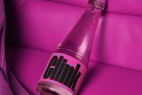 Pink bottle with bold black text Clink on a vibrant pink leather background showcasing bold typography and color contrast suitable for graphic designers.