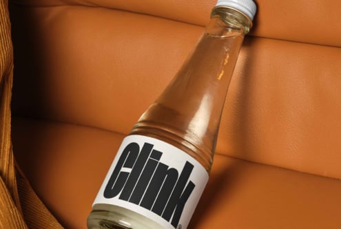 Glass bottle with bold typographic label Clink on orange leather surface Mockup perfect for product designers packaging branding SEO keywords design assets