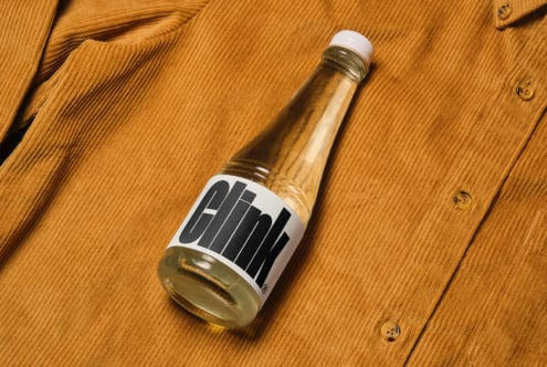 Glass bottle with Clink label on textured brown fabric background. Ideal for product mockup design, branding, and marketing. Professional asset for designers.