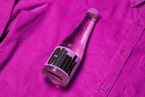 Pink corduroy fabric background with a stylish bottle showcasing modern typography on the label. Perfect for mockup design and branding projects.