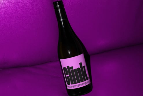 A modern wine bottle with bold Clink label on vibrant purple leather background ideal for branding mockups and graphic design projects.