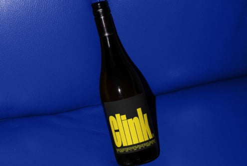 Wine bottle with bold yellow label reading Clink on blue leather background perfect for use in branding templates and graphic design mockups.