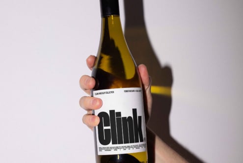 Hand holding a wine bottle with bold label design Clink perfect for packaging mockups and branding templates for designers seeking modern aesthetics.