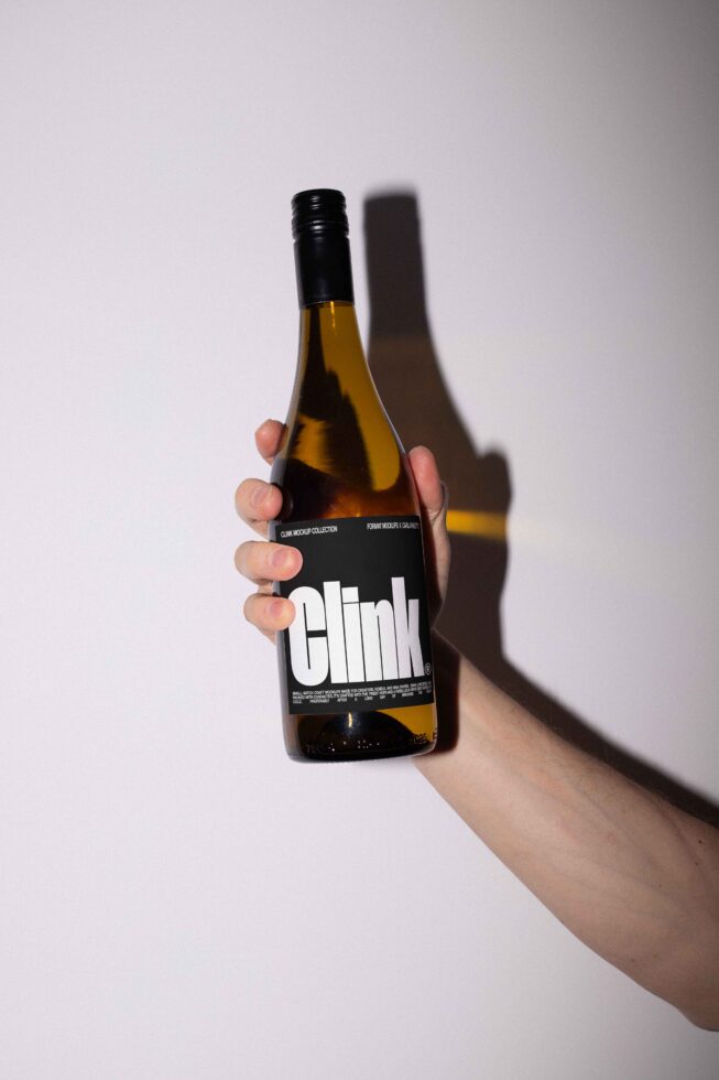 Hand holding a wine bottle with minimalist label design against a plain background perfect for product mockup showcasing custom labels or branding concepts.
