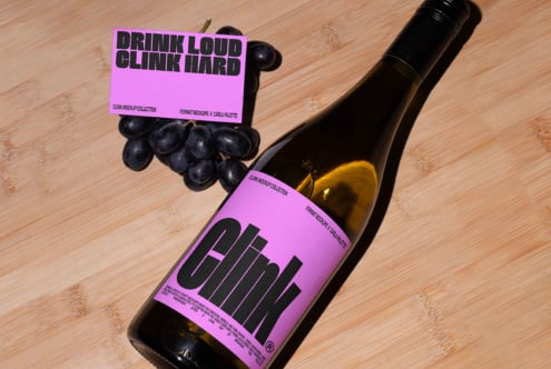 Wine bottle mockup with pink label on wooden surface, featuring a card and grapes. Perfect for designers looking for product branding templates.