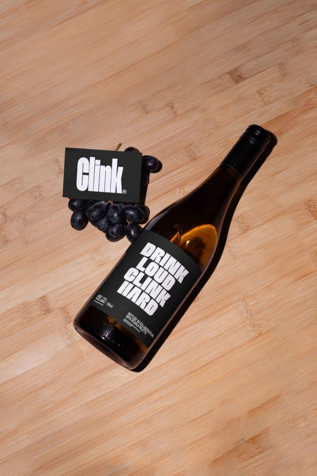 Wine bottle mockup with bold typography label on wooden surface, paired with grapes and branded card. Perfect for designers looking for beverage graphics.