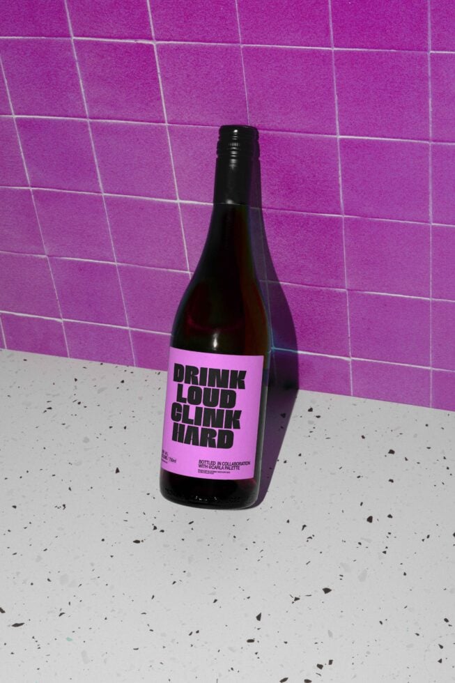 Wine bottle mockup with bold pink label design on terrazzo surface and purple tiled background ideal for branding and graphic design templates.
