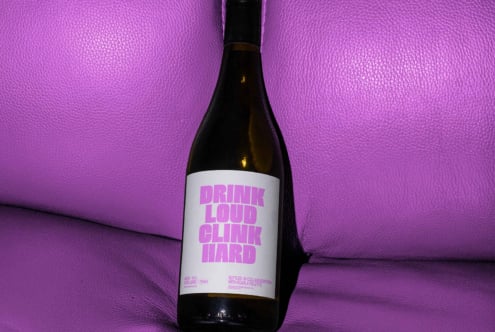 Wine bottle with modern label design on purple leather background. Typography: Drink Loud Clink Hard. Perfect for branding mockups and graphic design assets.