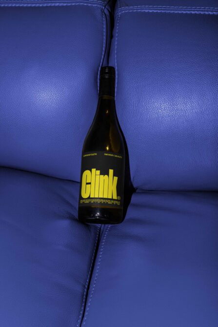 Beer bottle with yellow Clink logo on blue leather sofa, overhead shot