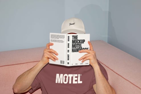 Man reading The Mockup Motel Handbook on sofa wearing cap and maroon t-shirt, design template, contemporary graphic style, creative designer asset.