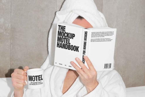 Person in a bathrobe reading The Mockup Motel Handbook with a coffee mug labeled Motel. Ideal for mockup templates, design inspiration, branding.