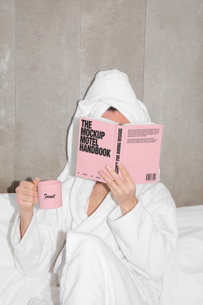 Designer reads Mockup Motel Handbook in cozy white bathrobe holding pink mug on bed Ideal for mockup design projects creative relaxation aesthetics