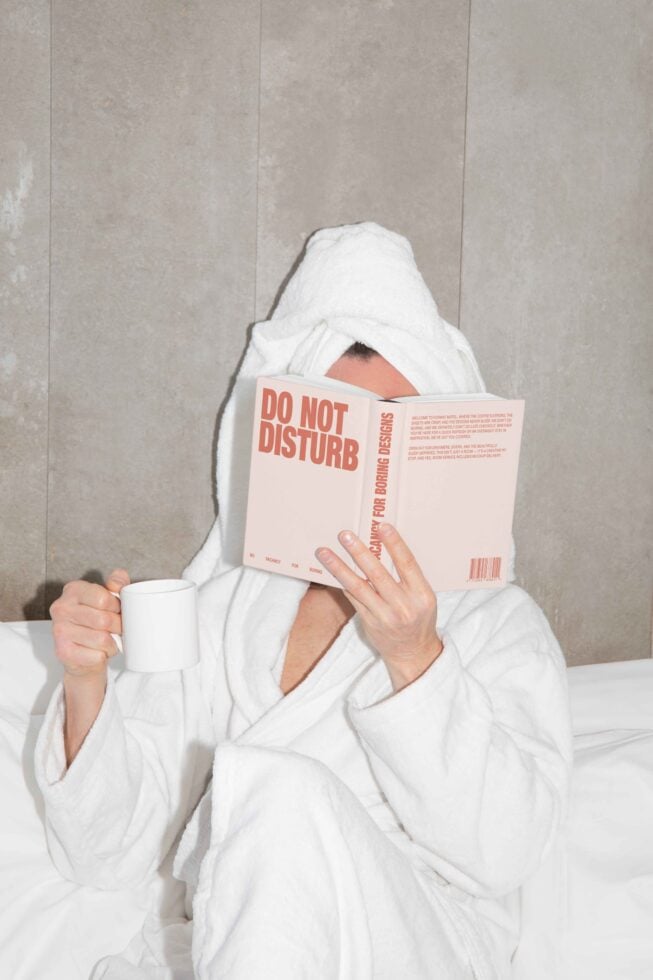 Person in a robe reads a 'Do Not Disturb' book while holding a mug. Perfect for mockups. Relaxed design inspiration lifestyle minimal setup.
