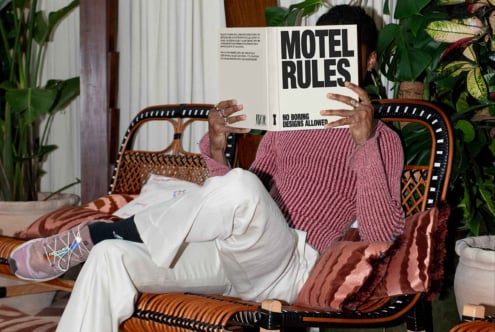 Designer reading book Motel Rules on a stylish wicker sofa surrounded by plants. Cozy setting for creative inspiration. Perfect for mockups and template visuals.