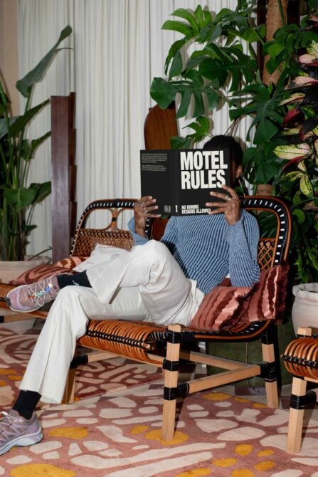 Person on rattan chair holding motel rules magazine with plants behind