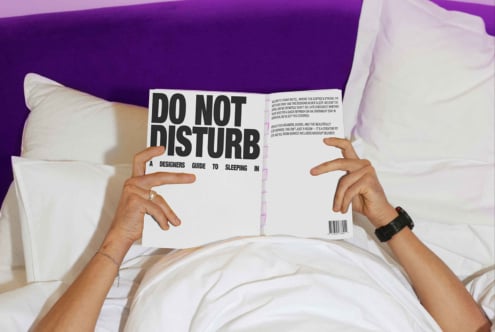 Designer reading Do Not Disturb book in bed with purple headboard and white pillows SEO keywords: mockup template font design guide sleeping creativity