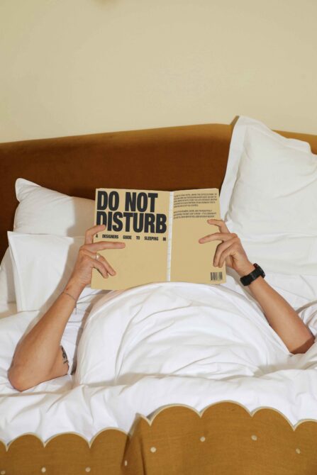 Person in bed reading do not disturb book with mustard headboard